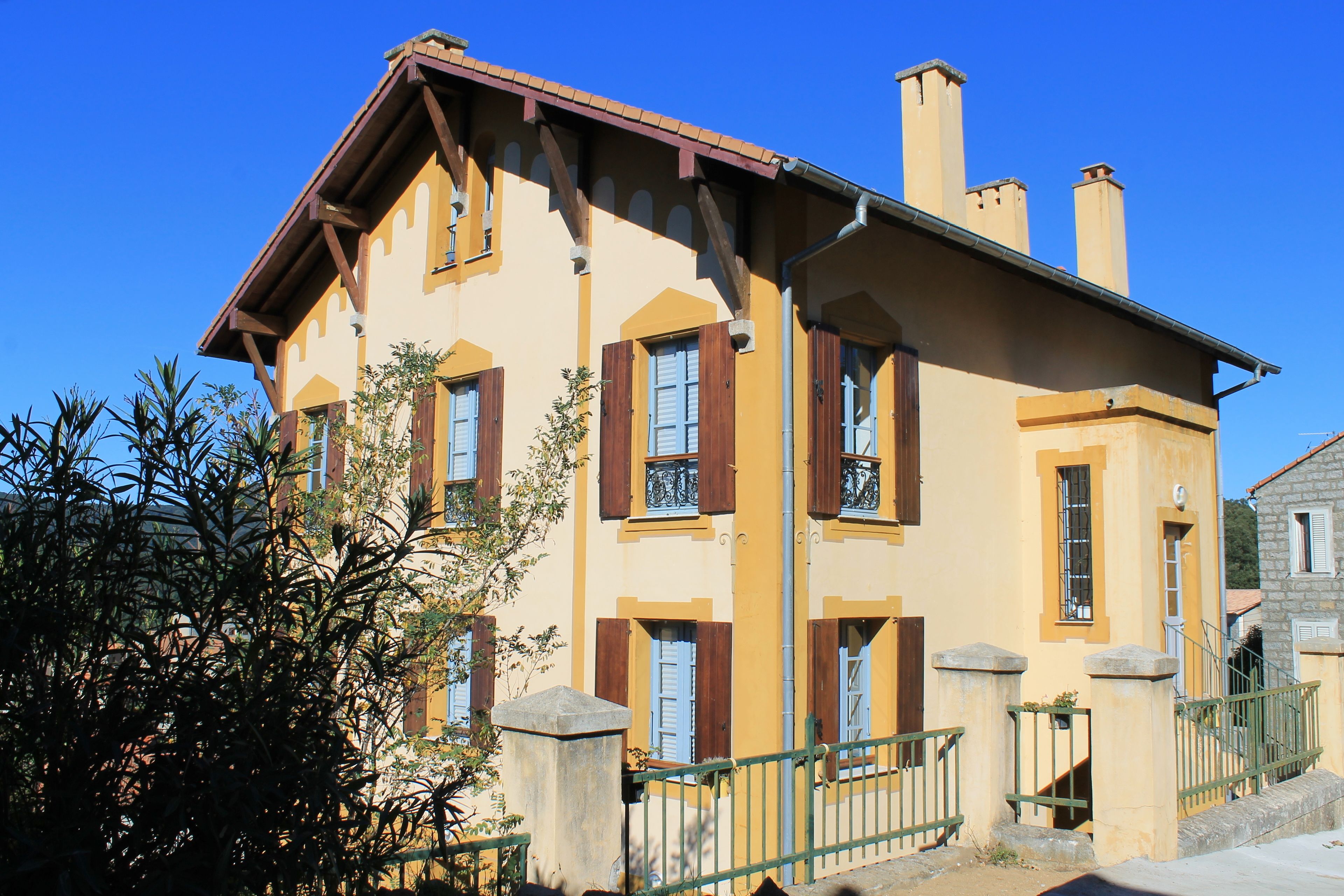 A two-story building with a yellow facade, wooden shutters, and a stone staircase leading to the entrance.