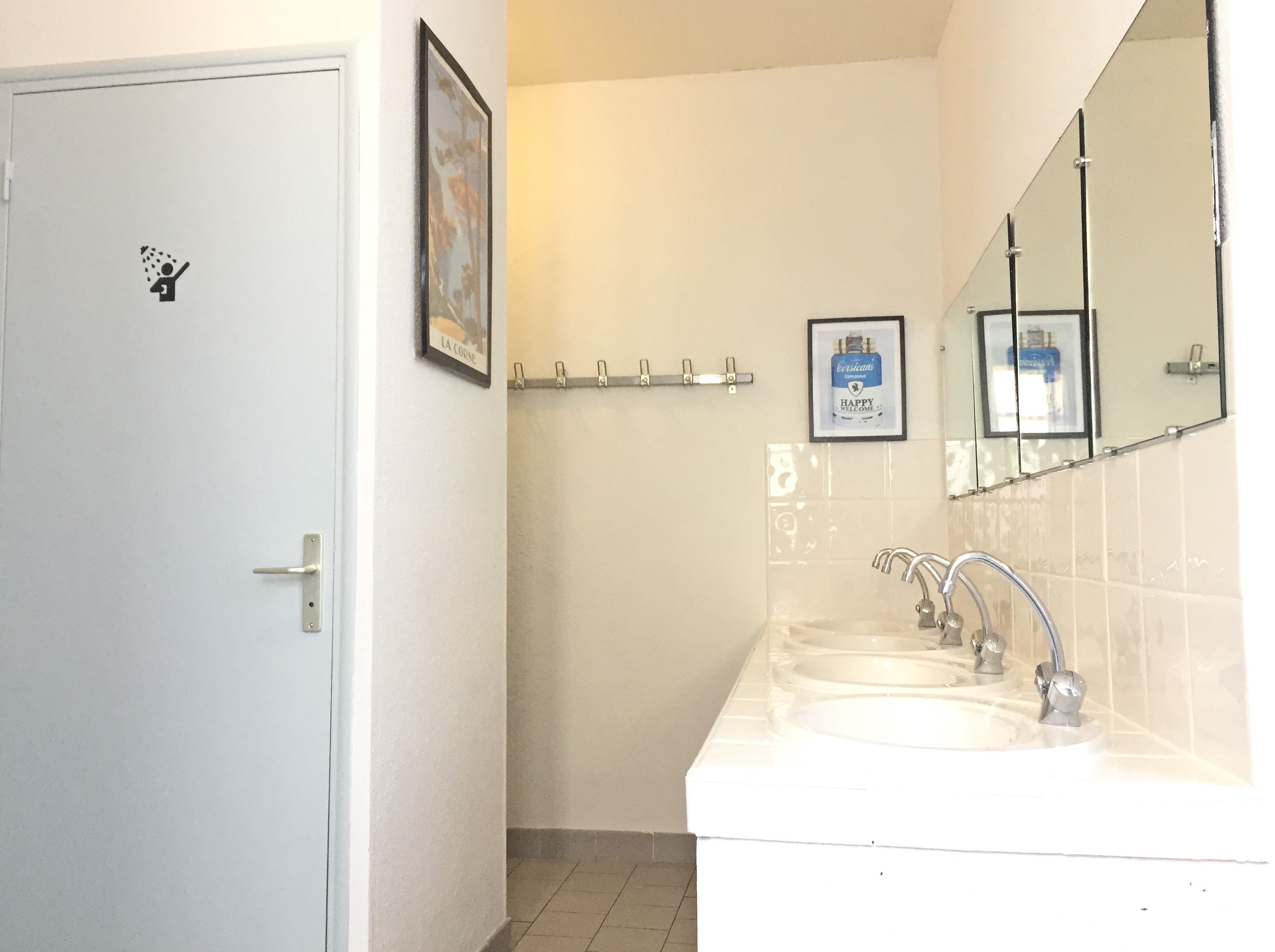 Un baño con una puerta blanca, un perchero, un cuadro enmarcado y un lavabo con espejo.