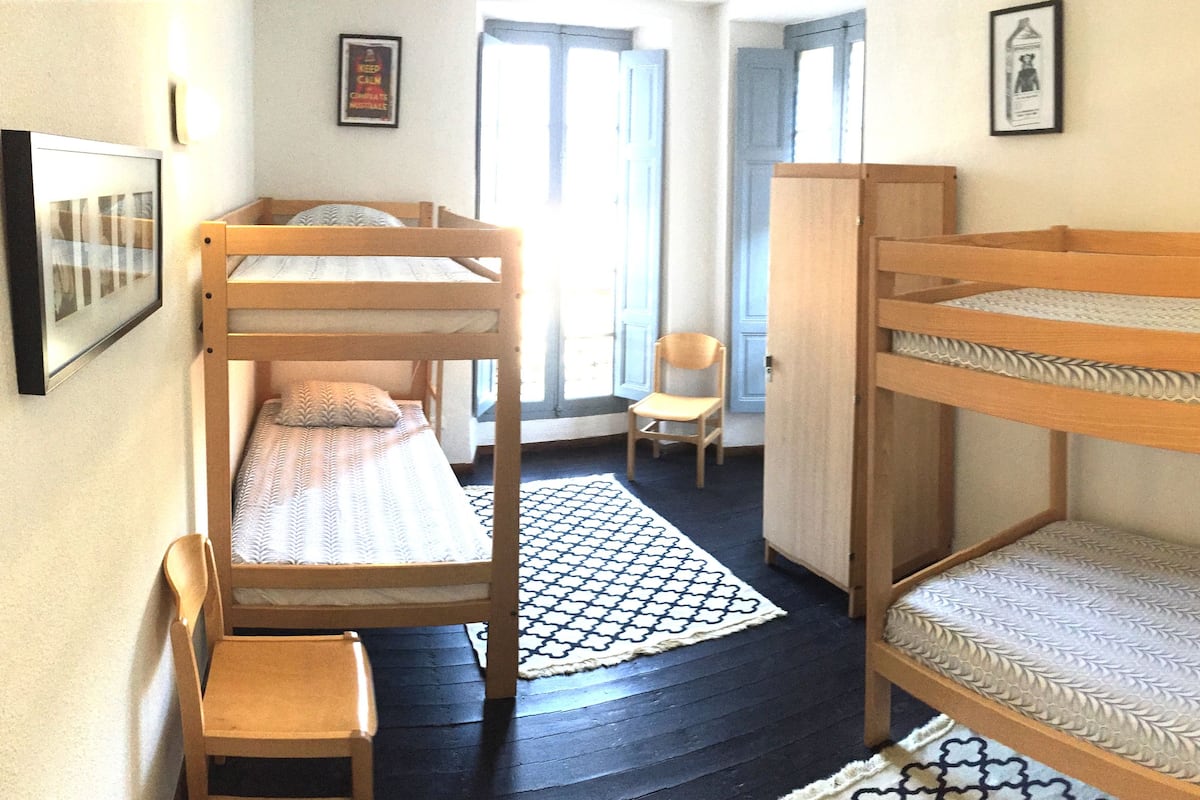 Una habitación con literas, una silla, un tapete estampado y cuadros en las paredes.