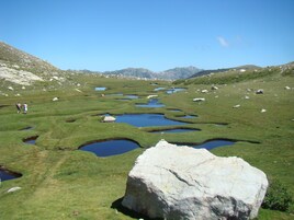 Un paisaje con praderas, varios estanques y una roca grande al frente.