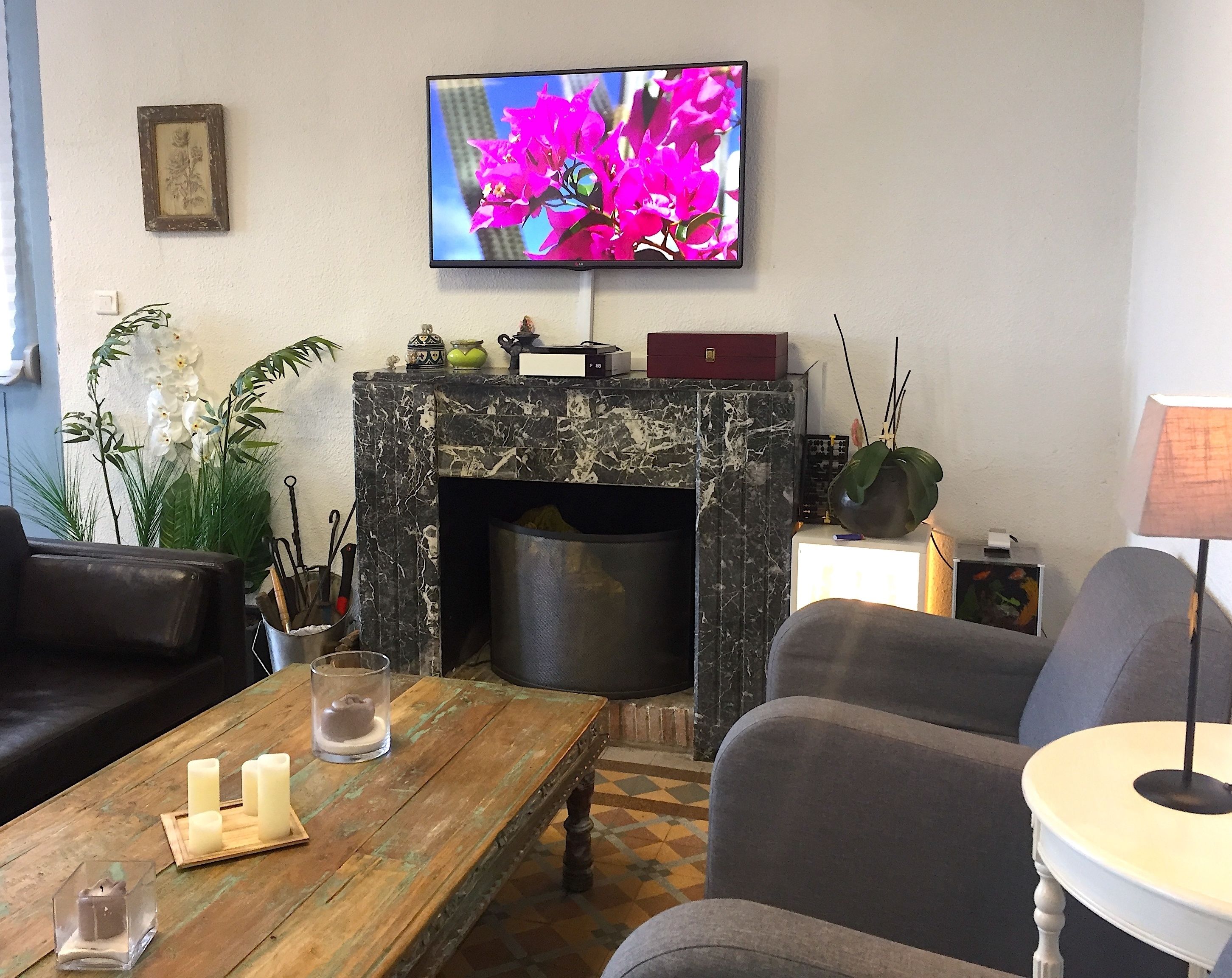 Een woonkamer met een open haard, een televisie erboven en een salontafel met kaarsen.