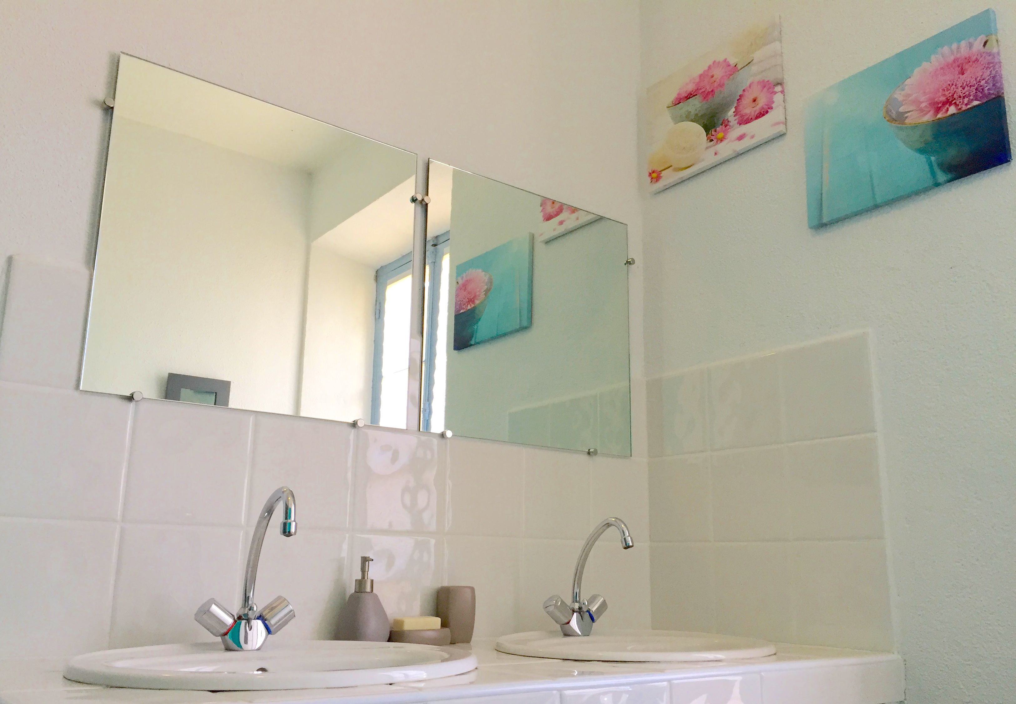 A bathroom with two sinks, a large mirror, and floral artwork on the wall.
