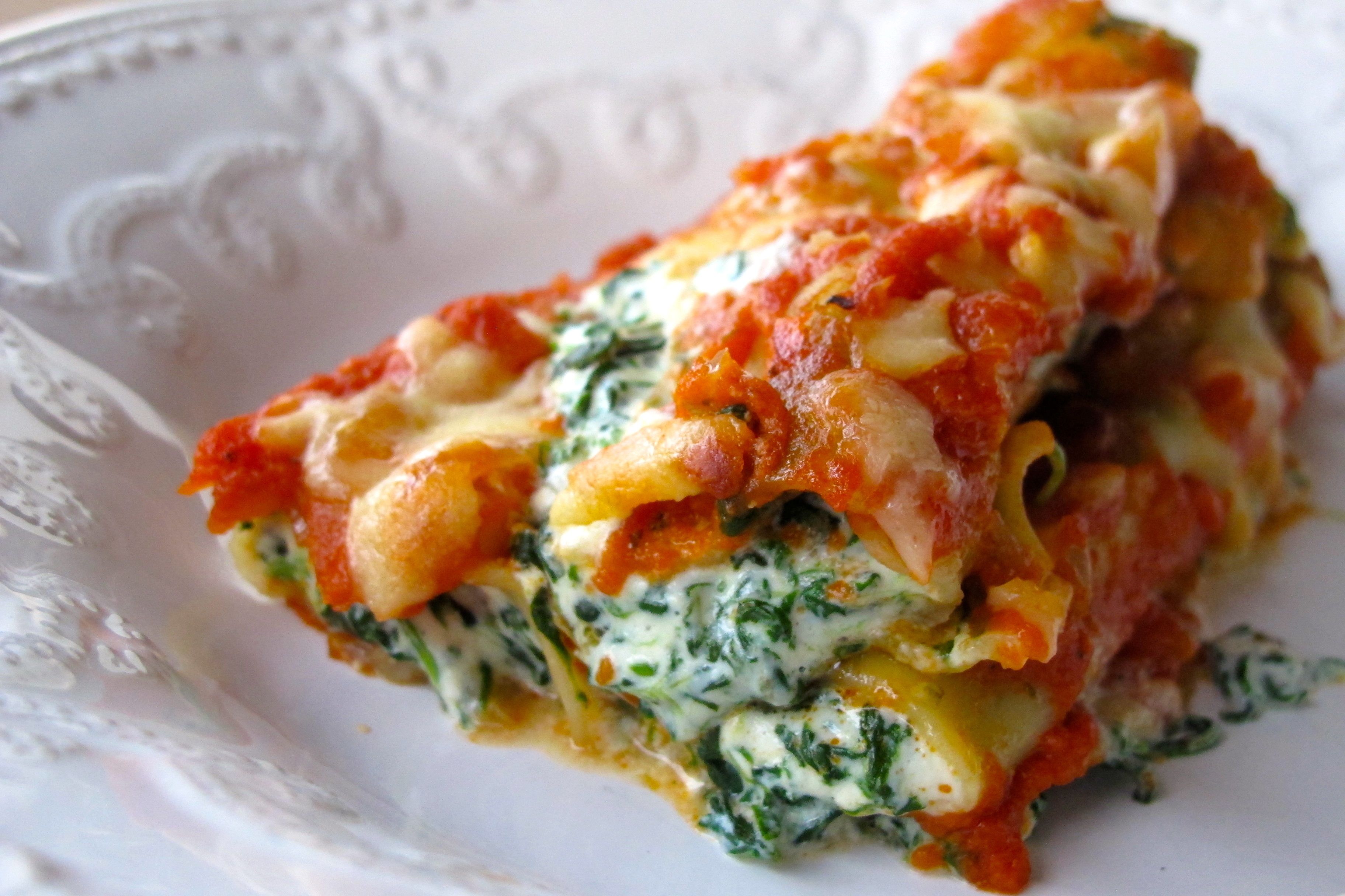 A close-up of a lasagna with spinach and cheese on a white plate.