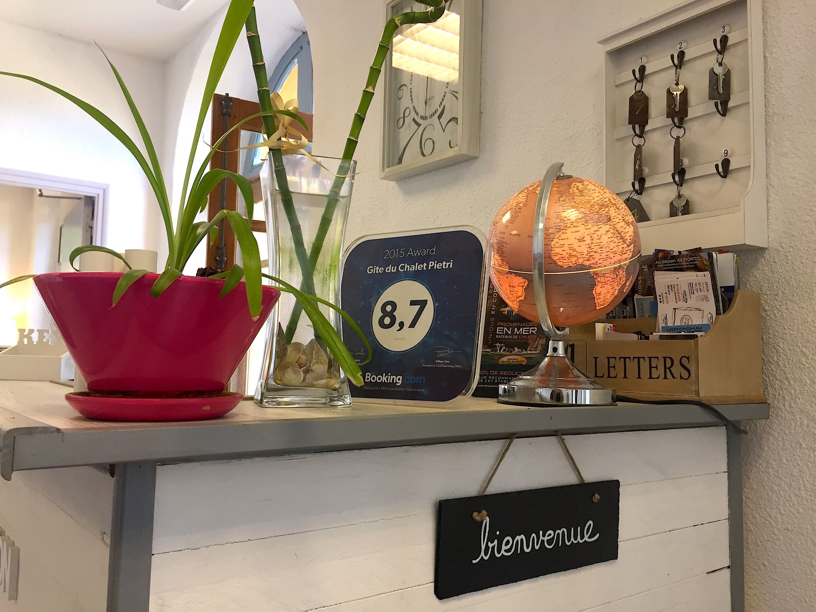 A reception desk with a red potted plant, a globe, a framed award plaque, and a welcome sign.