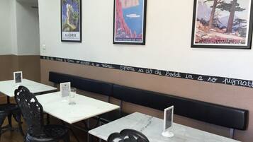 A restaurant interior with white marble tables and black metal chairs. There are framed posters on the wall, one of which reads "LA CORSE EN YACHT".