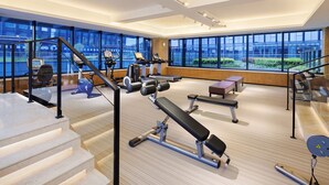 A modern gym with various exercise equipment, large windows, and a staircase.