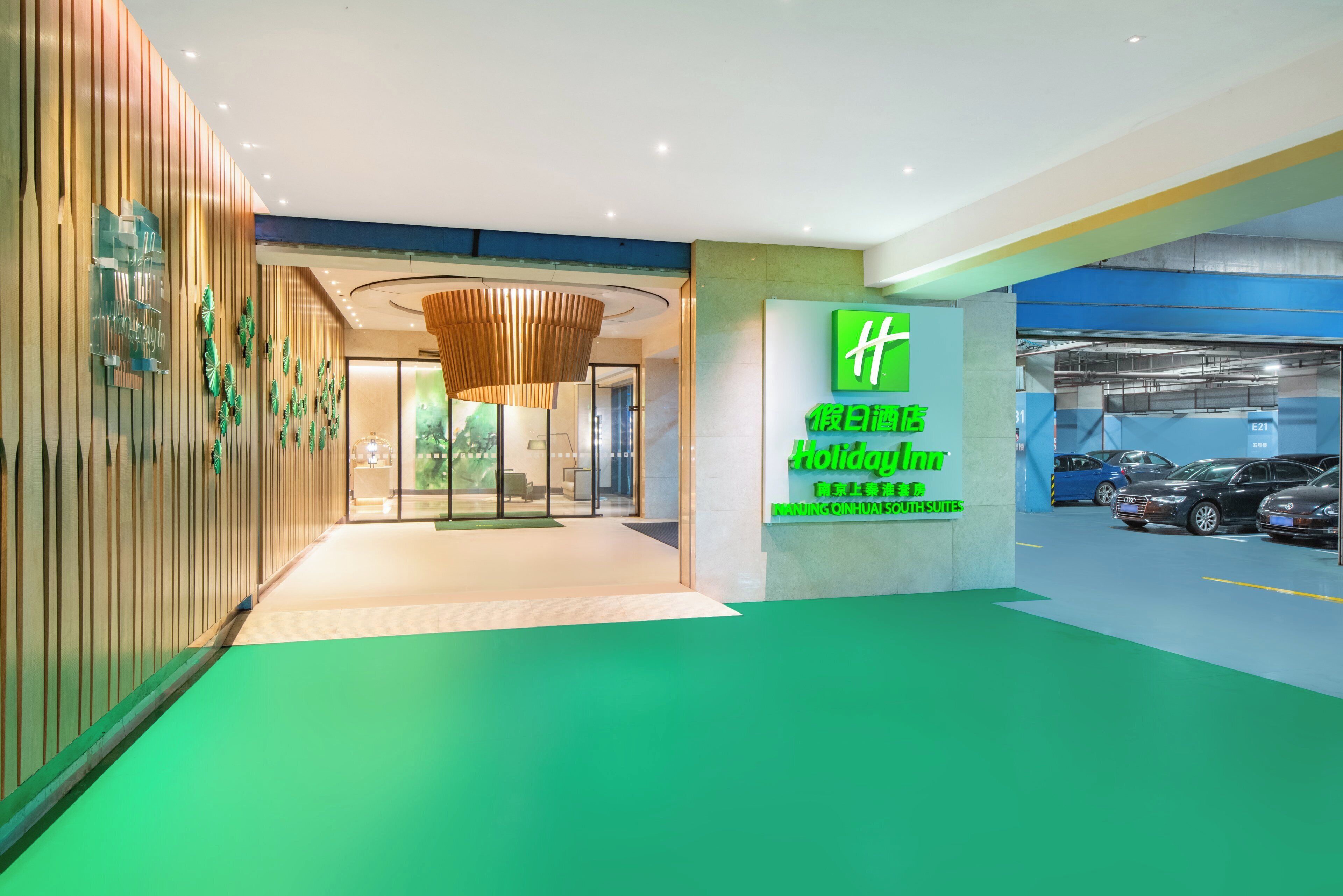 A hotel entrance with a green sign, a reception desk, and a parking area.