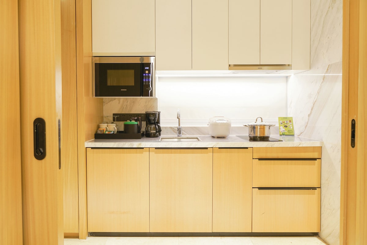 Una cocina moderna con armarios de madera, un microondas de acero inoxidable, una cafetera y un hervidor en la encimera.