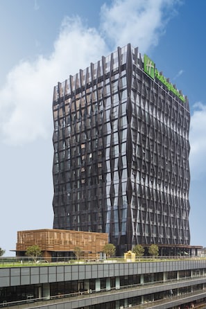 A modern building with a unique wavy facade, a green sign indicating it's a Holiday Inn Express, and a lower level with a covered walkway. - Holiday Inn Nanjing Qinhuai South Suites by IHG (Nanjing)