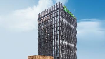 Un edificio moderno de gran altura con una fachada ondulada distintiva y un letrero verde llamativo que indica un hotel.