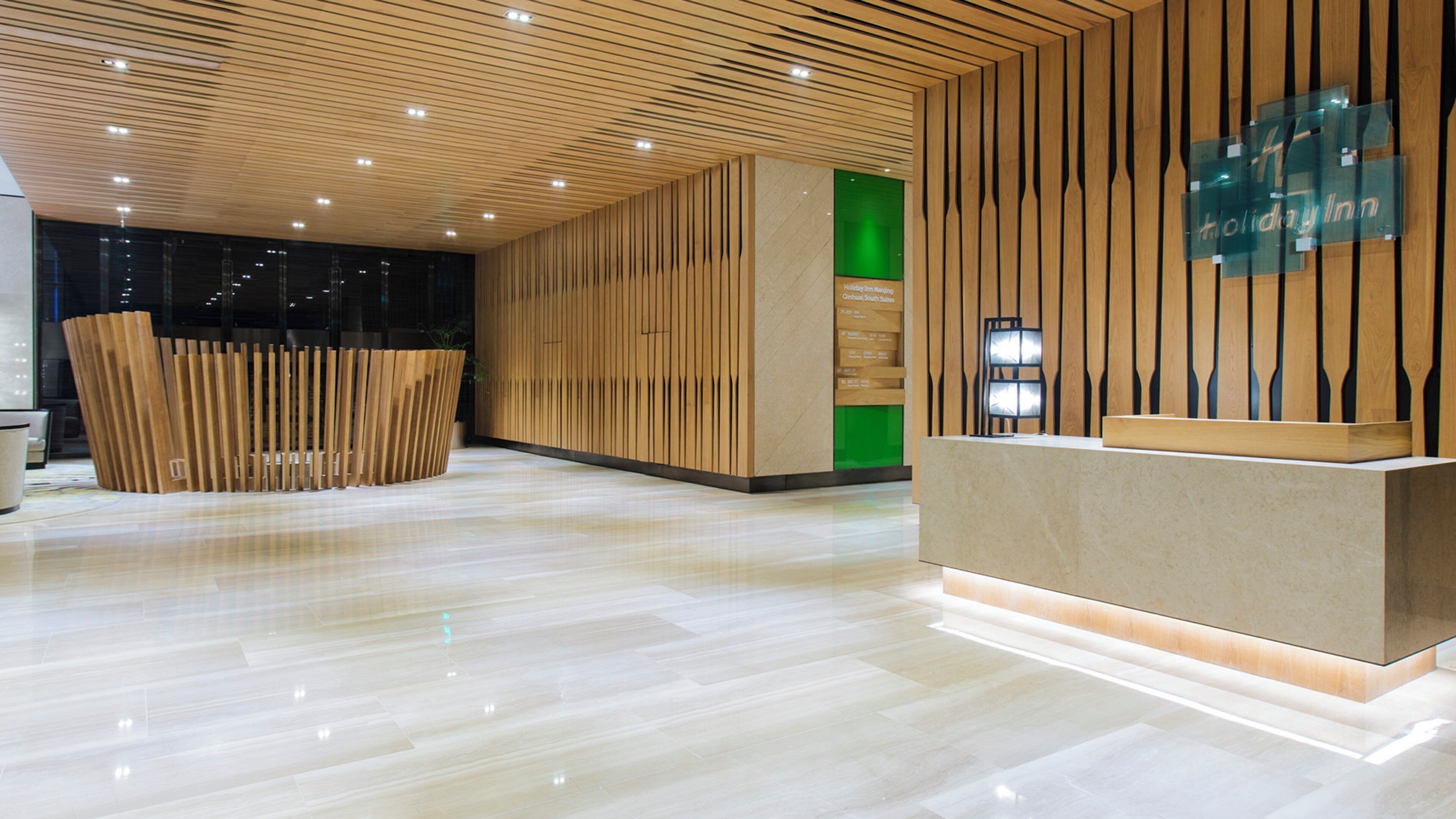 A modern hotel lobby with a wooden reception desk, a green accent wall, and a polished marble floor.
