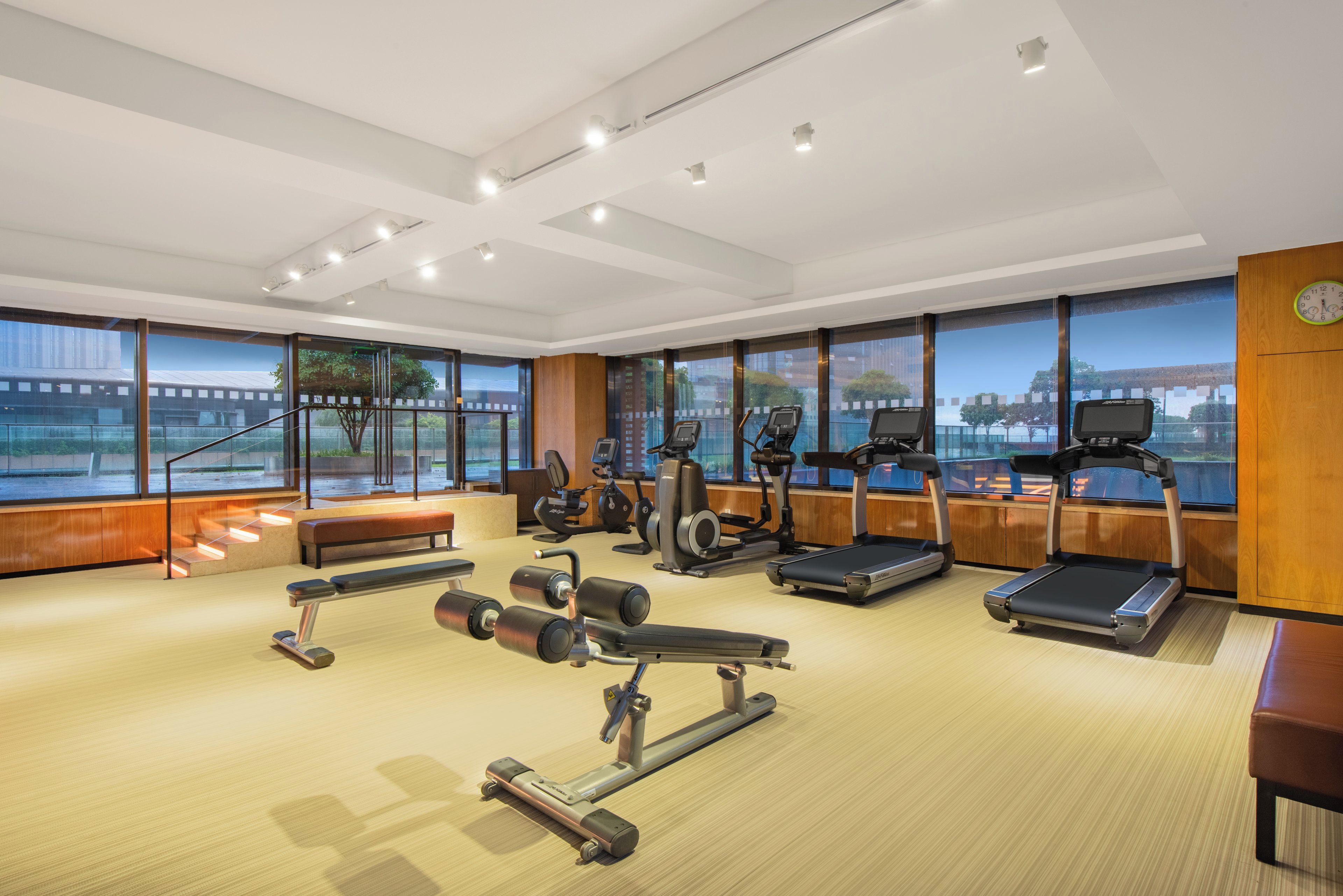 A modern gym with various exercise equipment, large windows, and a view of a bridge.
