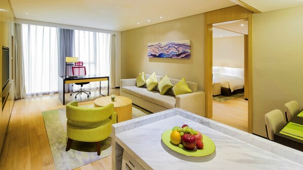 Ein Hotelzimmer mit einer Couch, einem Esstisch mit Früchten, einem Schreibtisch und einem Bett.