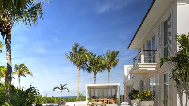 A swimming pool with lounge chairs and a covered seating area, surrounded by palm trees and a clear blue sky.