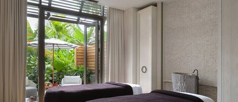A room with two beds, a sliding glass door to a garden, and a white chair.