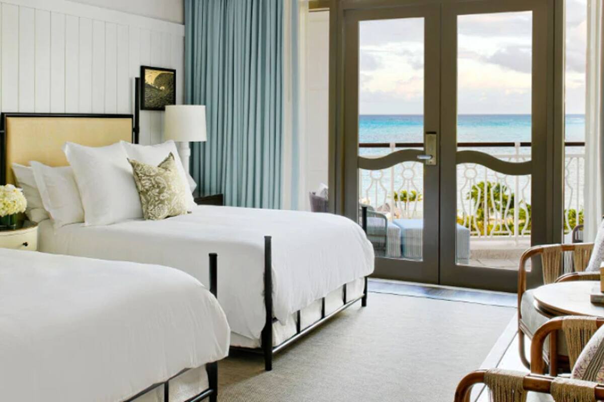 Een hotelkamer met twee bedden, een balkon met uitzicht op de oceaan en een zithoek met rieten meubilair.