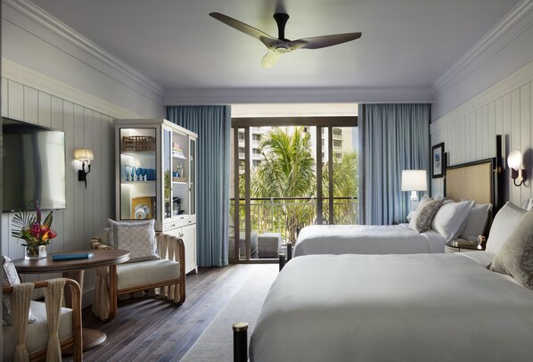 A hotel room with a bed, a desk, a chair, a TV, and a balcony with a view of palm trees.