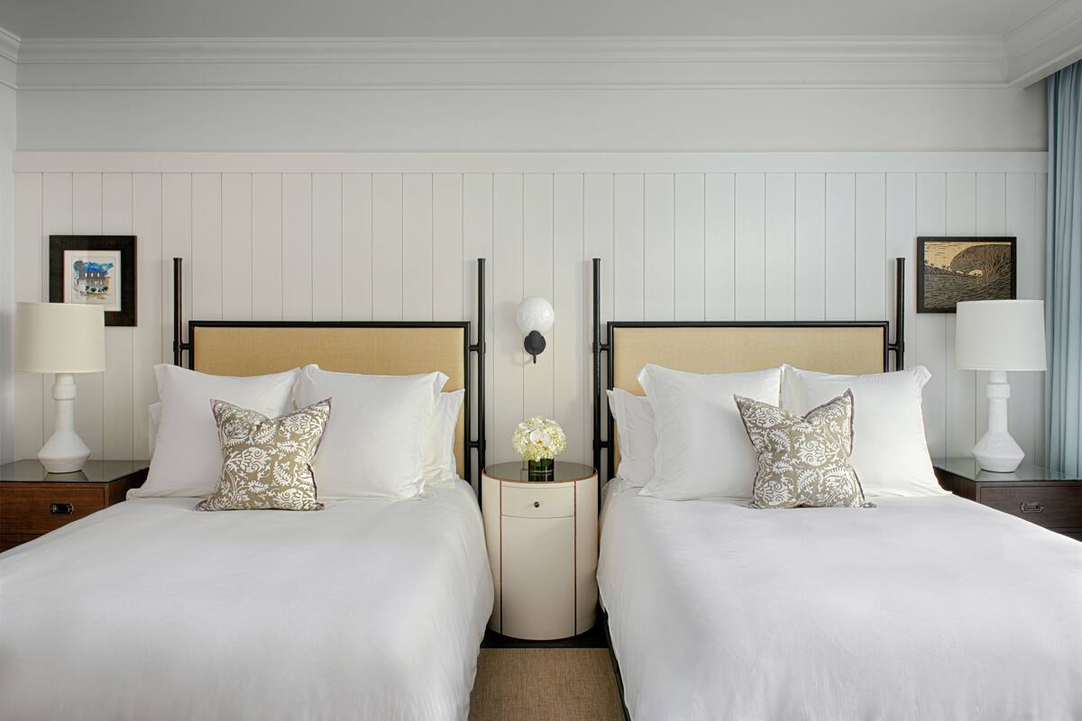Een hotelkamer met twee bedden, witte beddengoed en bijpassende nachtkastjes met lampen.
