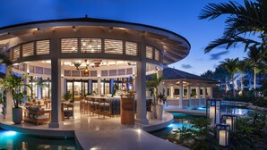 A modern, circular outdoor lounge area with a pool, surrounded by palm trees and well-lit with ambient lighting. - Rosewood Baha Mar (Nassau)