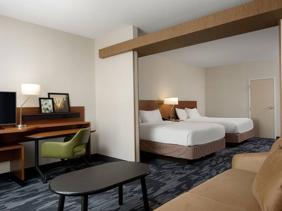 A hotel room with a desk, two beds, a TV, a chair, and a sofa.