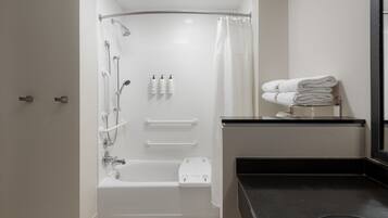 A modern bathroom with a walk-in shower, grab bars, a bathtub, and a toilet.