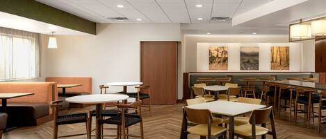 A modern restaurant with wooden flooring, round tables, and cushioned seating.