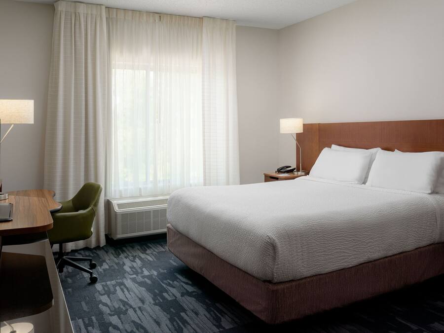 Una habitación de hotel con una cama grande, un escritorio con lámpara, una silla y una ventana con cortinas.