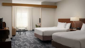 Habitación de hotel con dos camas, un escritorio, una silla, una lámpara y vistas al exterior a través de una ventana con cortinas.