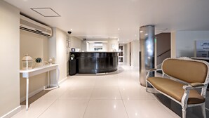 Ein Hotel-Empfangsbereich mit einer Rezeption, einer Sitzecke mit einem Sessel und einer Treppe.