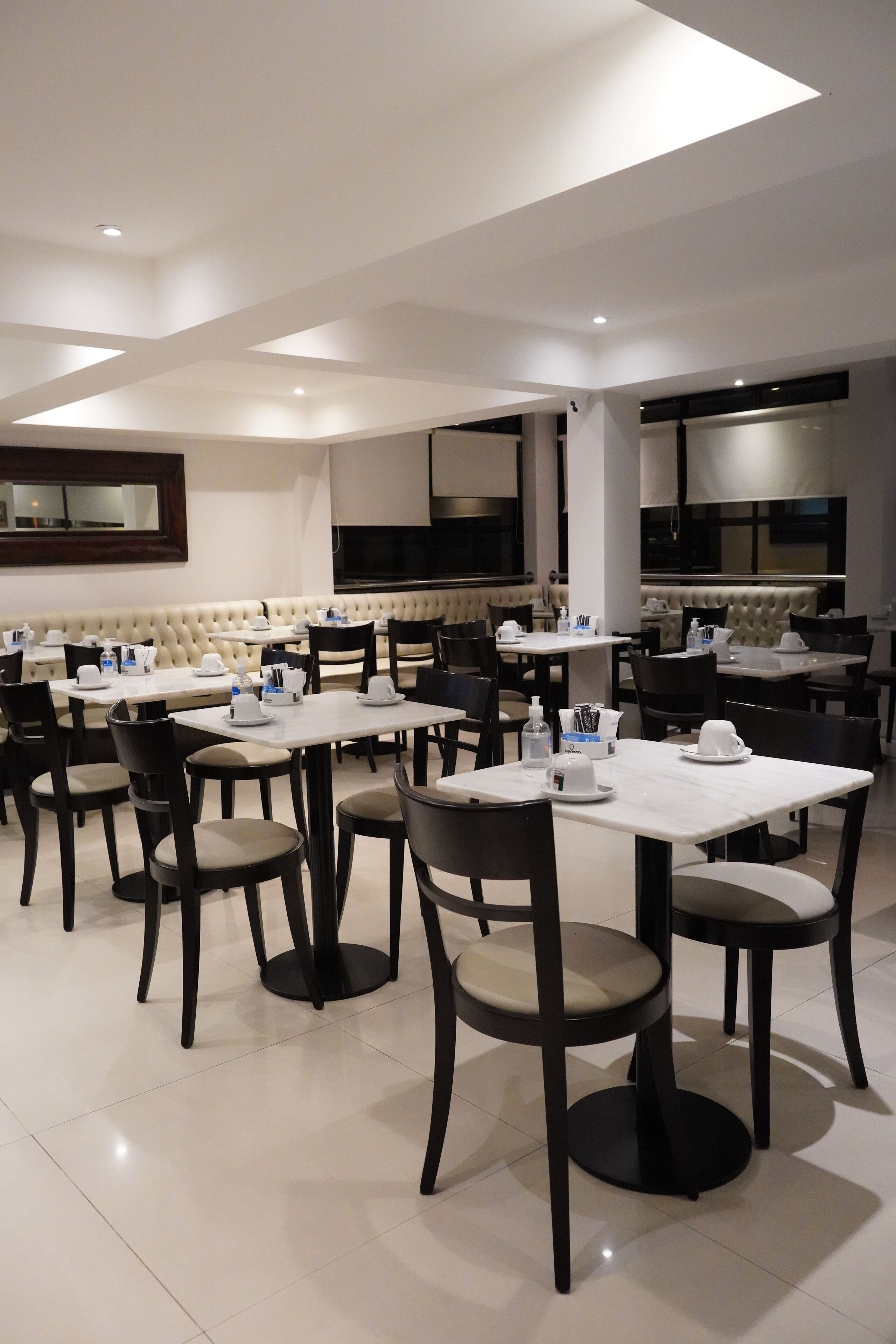 A modern dining area with multiple tables and chairs, a sofa, and a television screen.