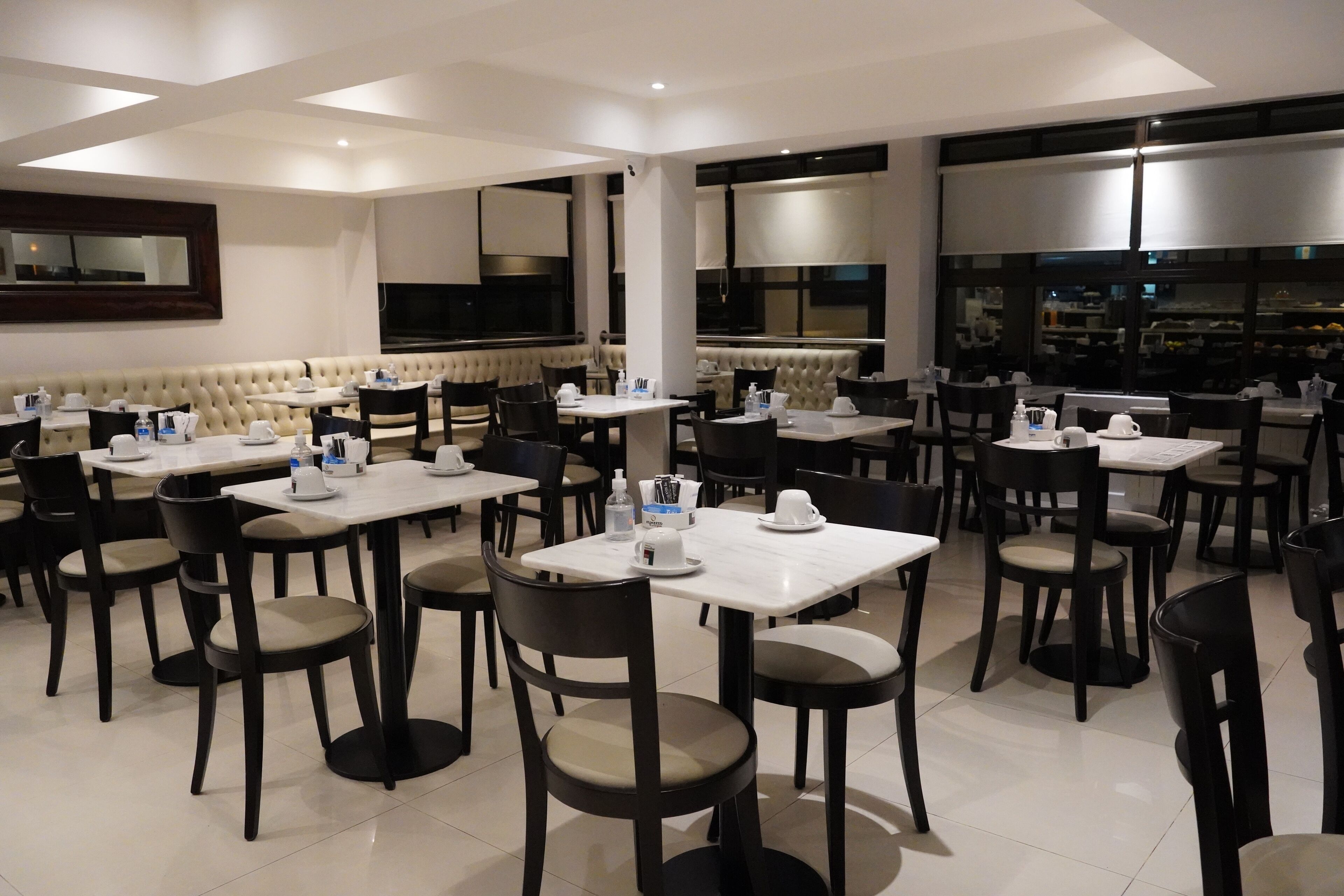 A modern dining area with multiple tables and chairs, a large cushioned bench, and a television screen.