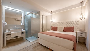 Ein modernes Schlafzimmer mit einem großen Bett, einer begehbaren Dusche, einem Schminktisch mit Spiegel und einer Kristallleuchtre.