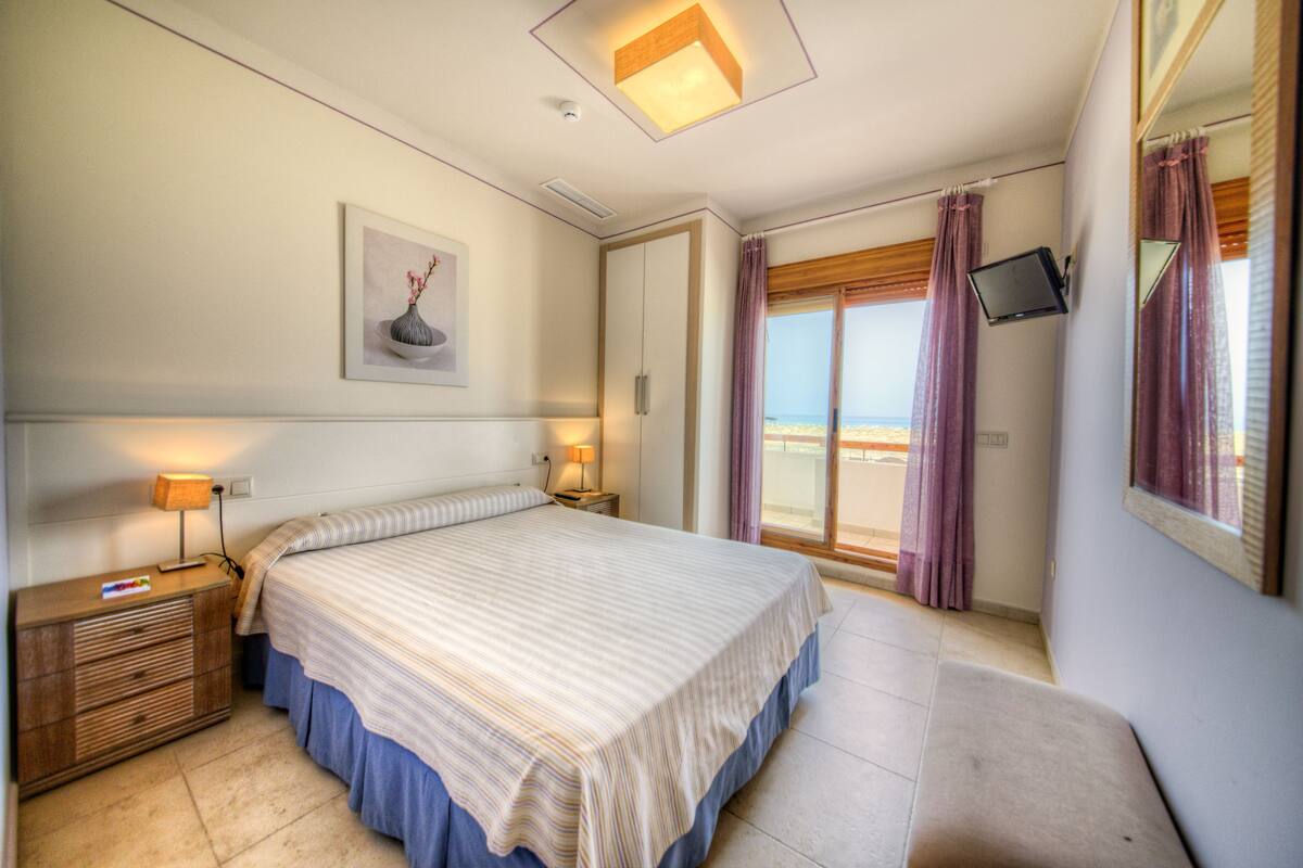 A bedroom with a bed, bedside tables, a TV mounted on the wall, and a window with curtains.