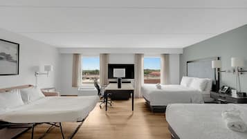 Habitación de hotel con dos camas, un escritorio, televisor y vistas a la ciudad.