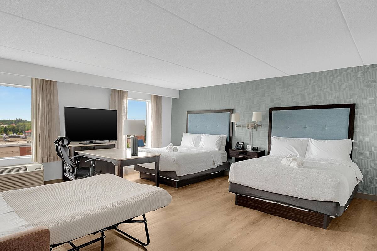 Une chambre d’hôtel avec deux lits, un bureau avec une télévision, une chaise et une vue sur l’extérieur.