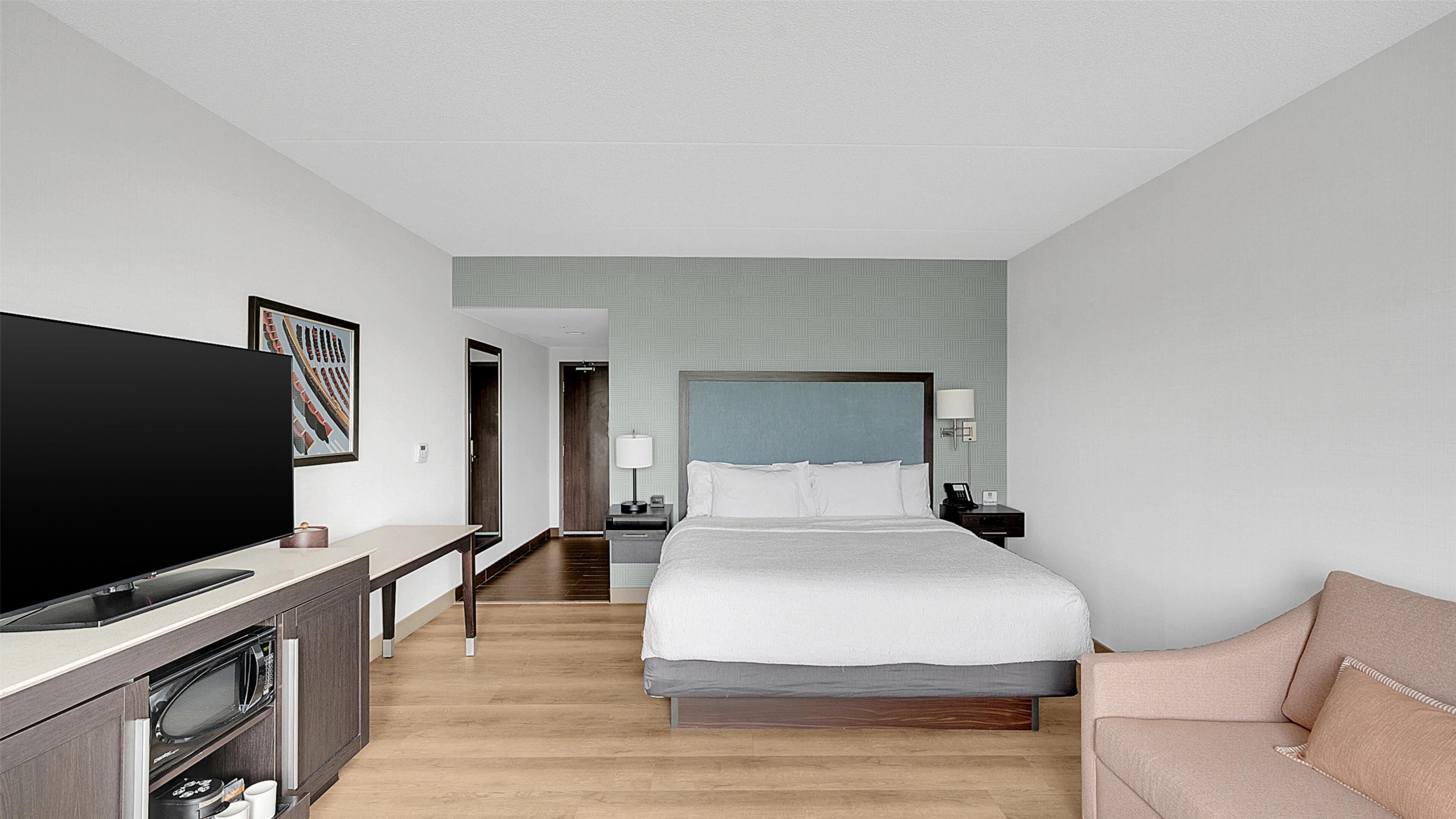 Quarto de hotel com cama, televisão, secretária com micro-ondas, sofá e porta que dá para outro quarto.
