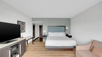 Quarto de hotel com cama, televisão, secretária com micro-ondas, sofá e porta que dá para outro quarto.
