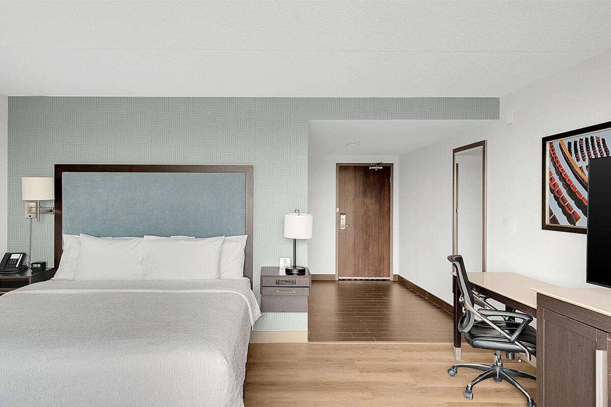 Une chambre d’hôtel avec un grand lit, des tables de chevet, un bureau avec une chaise, une télévision et une porte donnant sur une autre pièce.