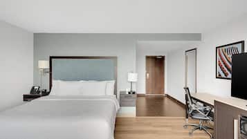 A hotel room with a large bed, bedside tables, a desk with a chair, a television, and a door leading to another room.