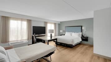 A hotel room with two beds, a desk, a chair, a television, a lamp, and a bedside table.