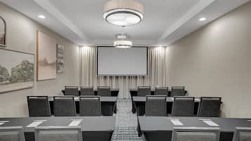 Un salón de conferencias con una pantalla grande, varias mesas y sillas.