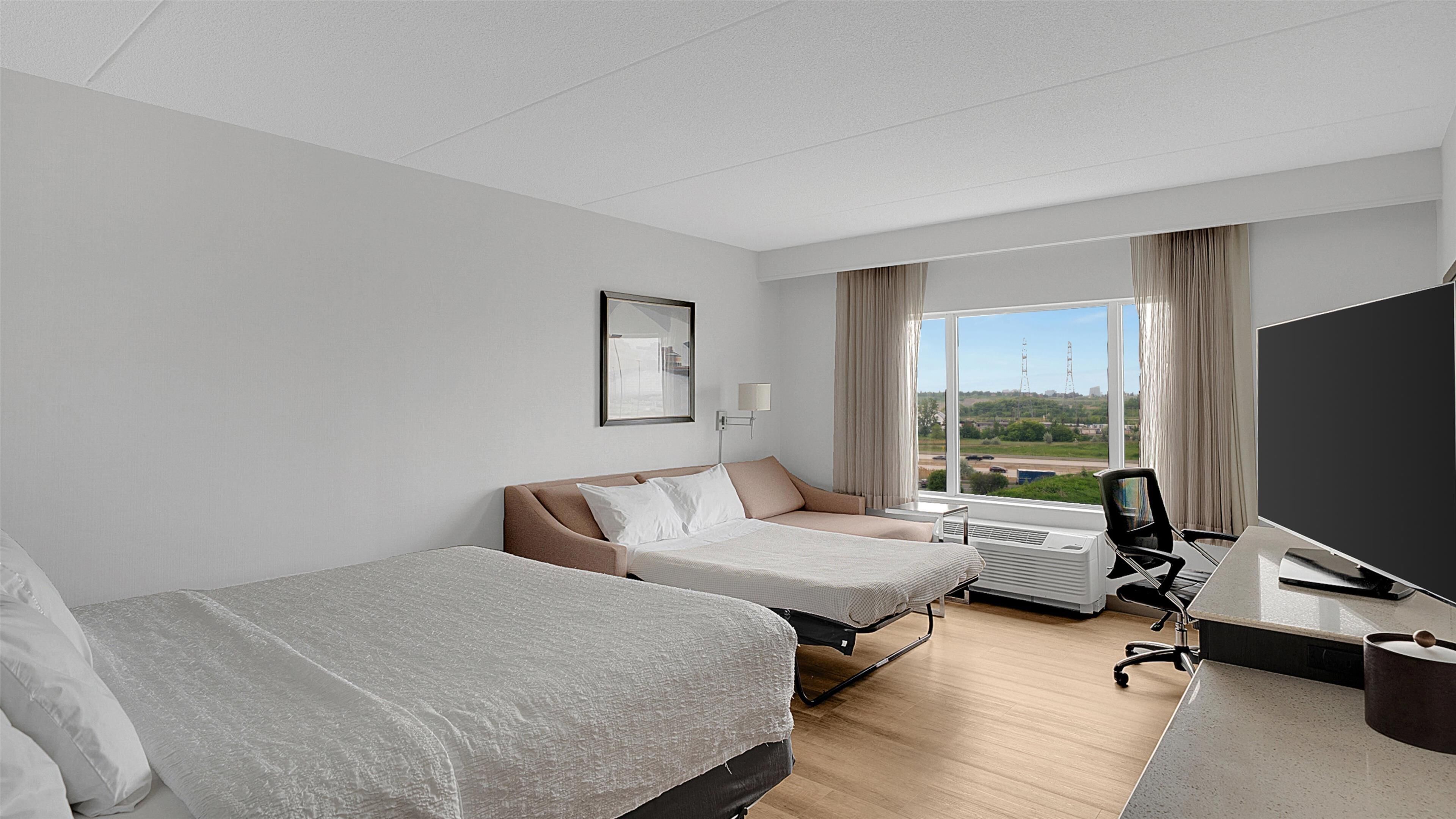 Une chambre d’hôtel avec deux lits, un bureau avec un ordinateur, une télévision et une fenêtre donnant sur un paysage urbain.
