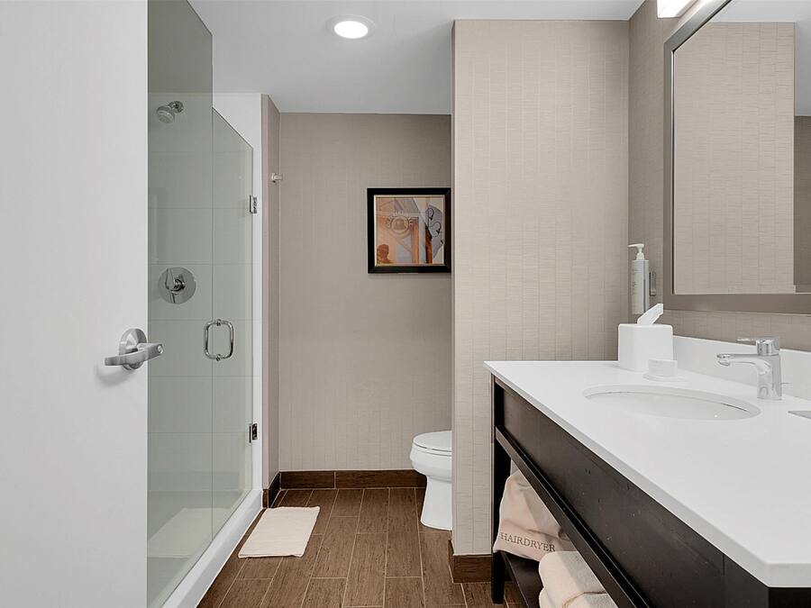 A modern bathroom with a glass-enclosed shower, a white sink with a large mirror, and a beige tiled wall.