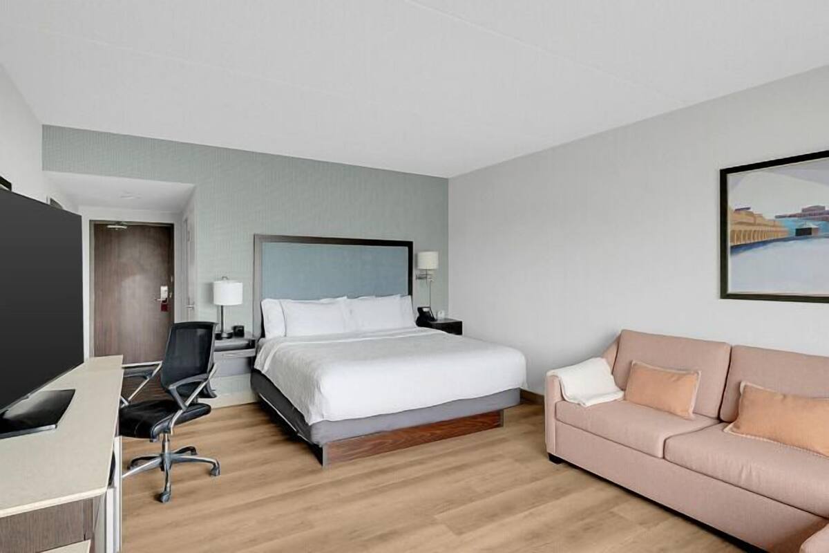 Une chambre d’hôtel avec un lit, un bureau, une chaise, un canapé et un tableau au mur.