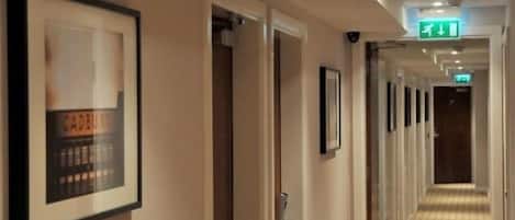 A hotel hallway with framed artwork on the walls, a carpeted floor, and doors leading to rooms.