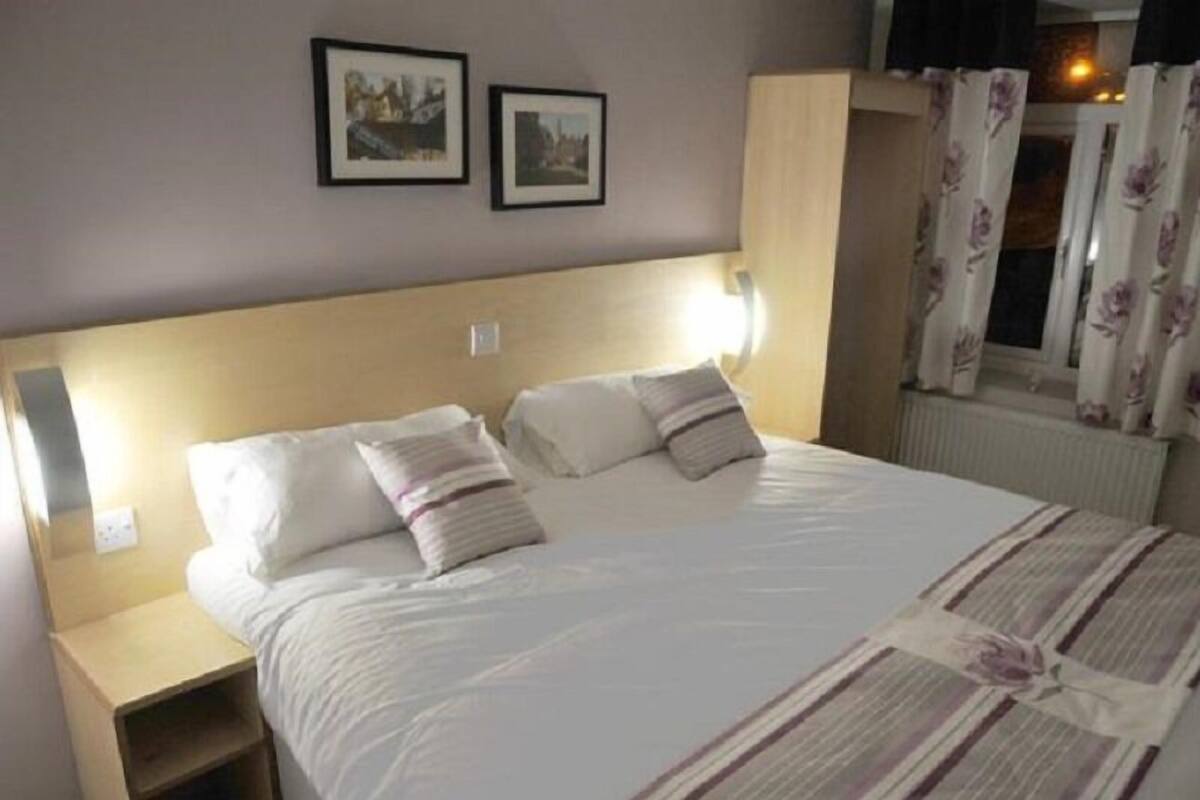 A neatly made bed with a striped blanket, a bedside table, and two framed pictures on the wall.