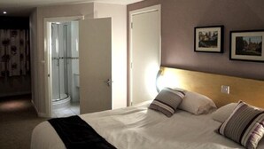 A bedroom with a bed, a bedside lamp, and a door leading to a bathroom. - The Royal George Hotel (Birmingham)