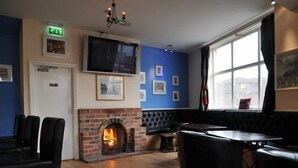 A cozy room with a brick fireplace, a television mounted on the wall, and a large window with curtains. - The Royal George Hotel (Birmingham)