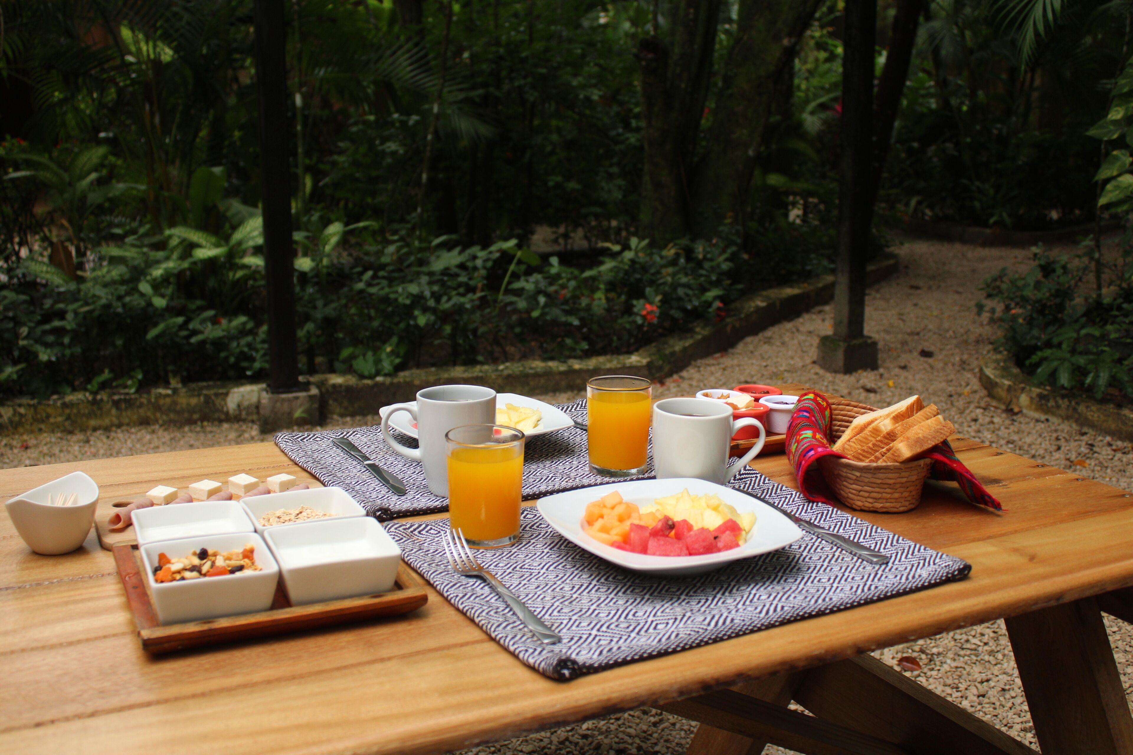Une table en bois dressée à l’extérieur pour le petit-déjeuner, avec une forêt en arrière-plan.
