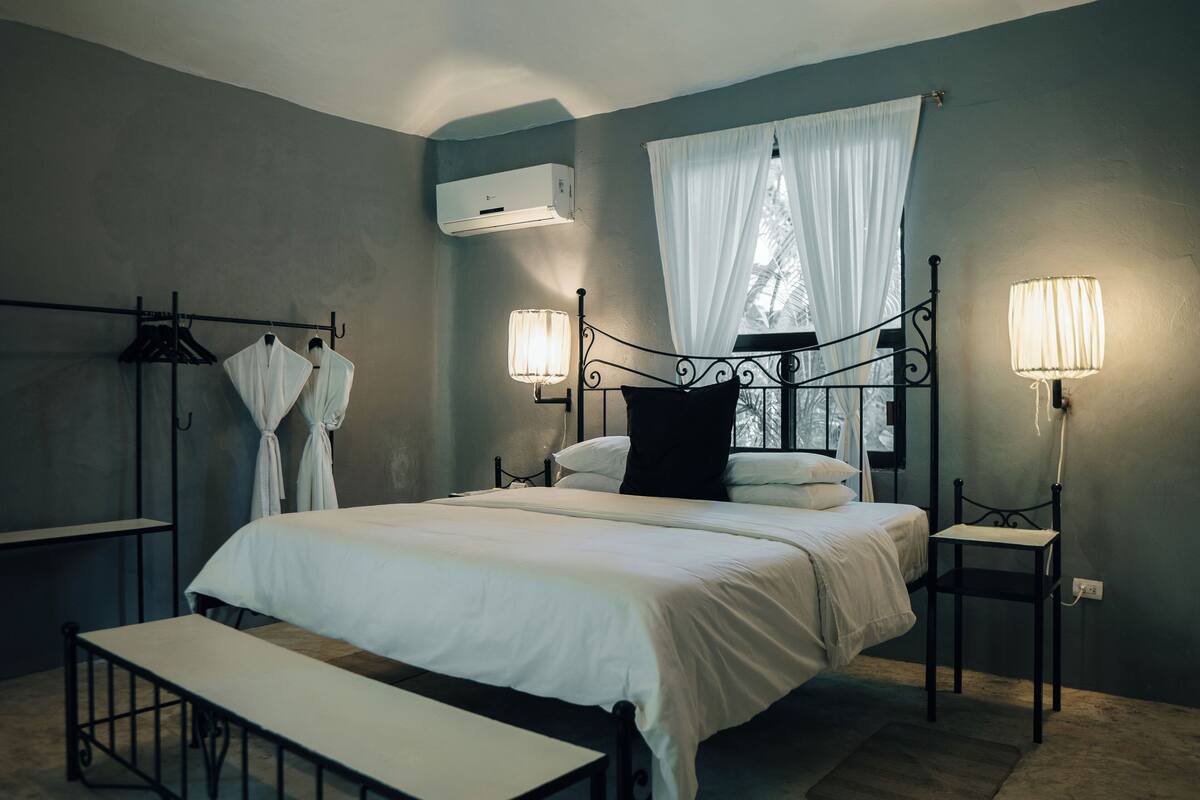 Ein Schlafzimmer mit Bett, Nachttischlampen, einer Bank, einem Kleiderschrank und einer Klimaanlage.